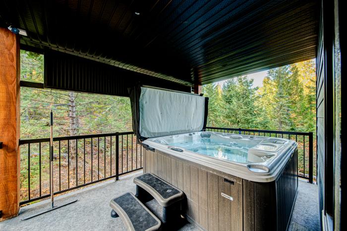 Covered private hot tub on the chalet deck surrounded by trees