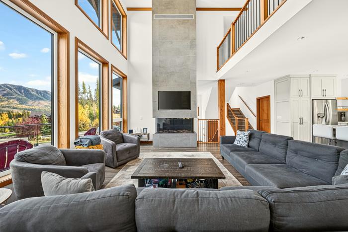 Open living room with sectional sofas, fireplace and floor-to-ceiling windows facing the mountains
